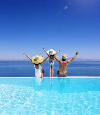 A happy family on summer holidays sits by the swimming pool and enjoys the beautiful view